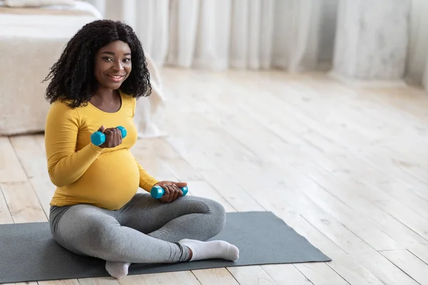 Усміхнена вагітна жінка займається з гантелями вдома — стокове фото