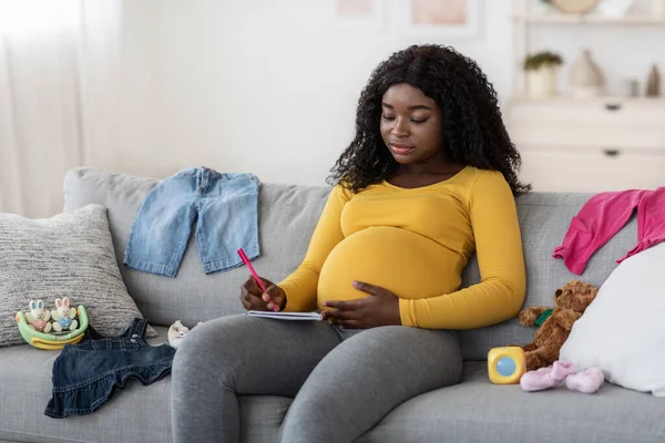 Концентрована вагітна жінка сидить на дивані з блокнотом і ручкою — стокове фото