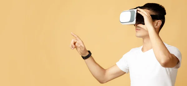 Serious young guy student in white t-shirt and virtual reality glasses touches to free space — Stock Photo, Image
