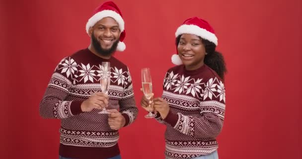 New Year party. Young happy black couple in xmas hats dancing with champagne over red studio background — Stock Video