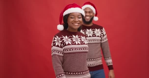 Молодой африканский американец приходит к своей девушке и закрывает глаза, играя Peekaboo Рождественская игра, красный фон — стоковое видео