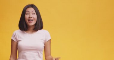 Heyecanlı Asyalı kadının harika bir fikri var, ilham alıyor, turuncu stüdyo arka planında duruyor ve boş alanı var.