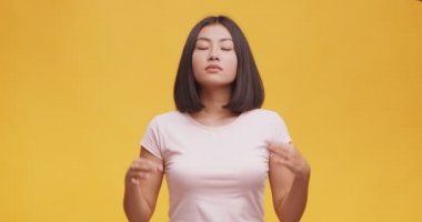 Genç Asyalı bayan meditasyon yapıyor, sakin ve rahat hissediyor, ellerini Mudra jestinde tutuyor ve gülümsüyor, turuncu arka plan