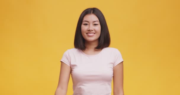 Nette junge asiatische Frau gestikuliert Ok-Zeichen und lächelt, orange Studio Hintergrund — Stockvideo