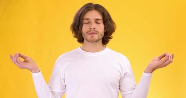 Studio portrait of young man meditating, opening his eyes and breathing deeply with mudra om, orange background — Stock Video