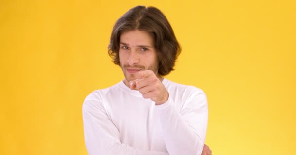 Młody zabawny facet celujący w kamerę i pokazujący gest telefonu, flirtujący z tobą nad pomarańczowym tłem studia — Wideo stockowe