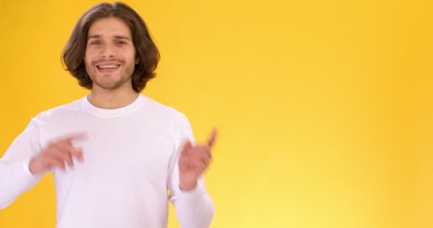 Happy excited guy pointing playfully at empty space and smiling approvingly, orange studio background — Stock Video