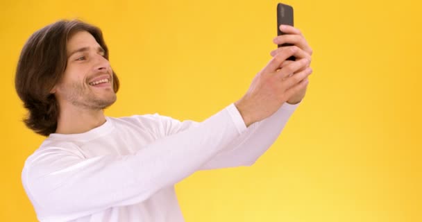 Νεαρός βγάζει selfie σε smartphone, ποζάρει σε mobile camera, πορτοκαλί φόντο στούντιο — Αρχείο Βίντεο