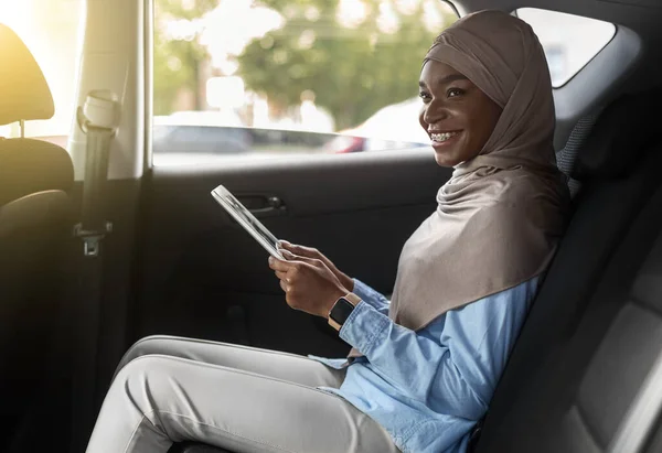 Zwart moslim ondernemer vrouw met behulp van digitale tablet op de achterbank in de auto — Stockfoto