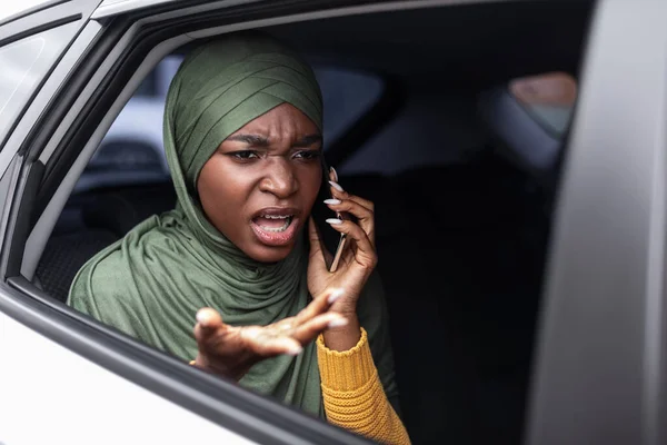 Mujer negra musulmana disgustada hablando en el celular en el asiento trasero en el coche — Foto de Stock