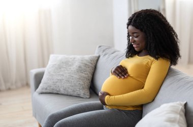 Joyful black pregnant woman hugging her big tummy, side view