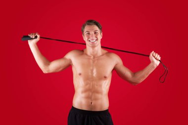 Kırmızı stüdyo arka planında atlama ipi tutan kaslı, gülen milenyum çocuğu.