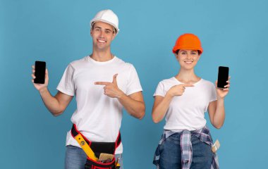 Koruyucu kasklı mutlu çift siyah ekranlı akıllı telefonlara bakıyor.