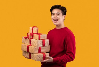 Mutlu Asyalı genç adam elinde hediye kutuları tutuyor.
