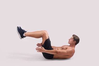 Gömleksiz güçlü bir adamın karın kasları egzersizi yapması, vücut kaslarını ışık stüdyosu arka planı üzerine çalıştırması.