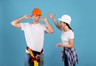 Tadilat sırasında tartışan kasklı bir çift, parmaklarıyla kulaklarını tıkayan sinirli bir adam.