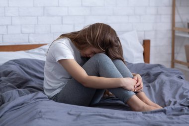 Depresyondan muzdarip mutsuz genç bir kadın, yüzünü gizliyor ve evde yatakta ağlıyor.