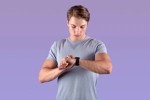 Pria atletis yang kuat melihat jam tangan pintarnya dengan latar belakang studio ungu — Stok Foto