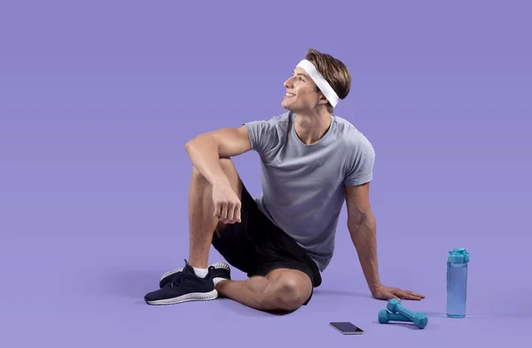 Pria muda atletik dalam pakaian olahraga beristirahat setelah bekerja di latar belakang studio ungu, potret panjang penuh — Stok Foto