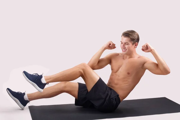 Fuerte chico joven haciendo ejercicio en la alfombra deportiva, trabajando en los músculos abdominales sobre fondo de estudio de luz, espacio de copia —  Fotos de Stock