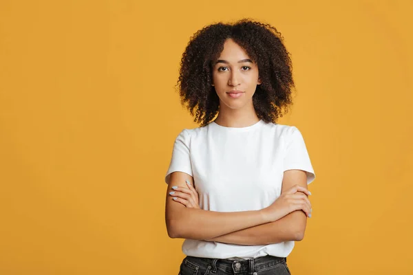 Mujer afroamericana joven y confiada seria con el pelo rizado en camiseta blanca con brazos cruzados — Foto de Stock