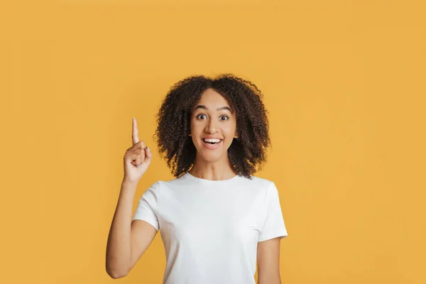Bra idé eller bra erbjudande. Leende glad ung afrikansk amerikansk kvinna i vit t-shirt pekar finger upp — Stockfoto