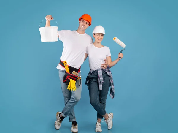 Painters couple standing with paint bucket and roller brush on blue background — 图库照片