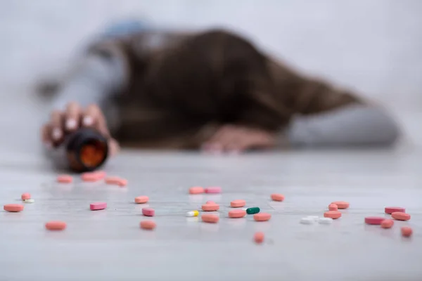 Młoda kobieta popełniająca samobójstwo, leżąca na podłodze z tabletkami rozrzuconymi ze słoika, wybiórczo skupiona — Zdjęcie stockowe