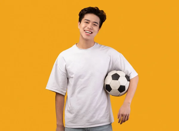 Pria Asia berpose dengan bola sepak di latar belakang oranye — Stok Foto