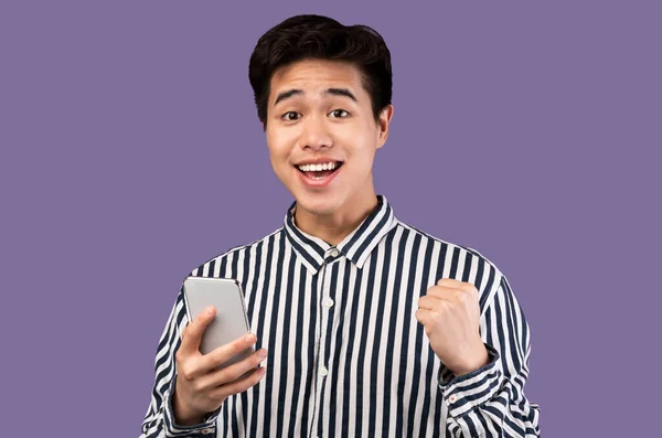 Захоплений азіатський хлопець використовує мобільний телефон, святкуючи онлайн виграш — стокове фото