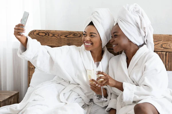 Senhoras felizes em roupões de banho sentados na cama e tomando selfie — Fotografia de Stock