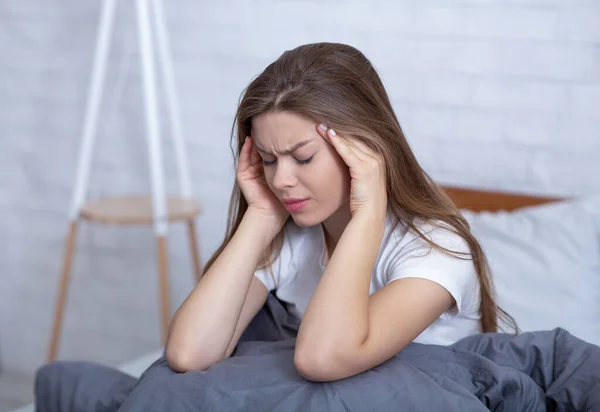 Depresyondaki genç bir kadın baş ağrısı ya da yatakta stres atmak için şakaklarına masaj yapıyor. — Stok fotoğraf