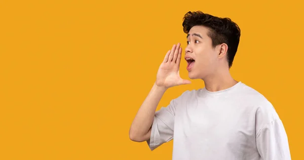 Asiático hombre celebración palma cerca boca, gritando a un lado en copyspace —  Fotos de Stock