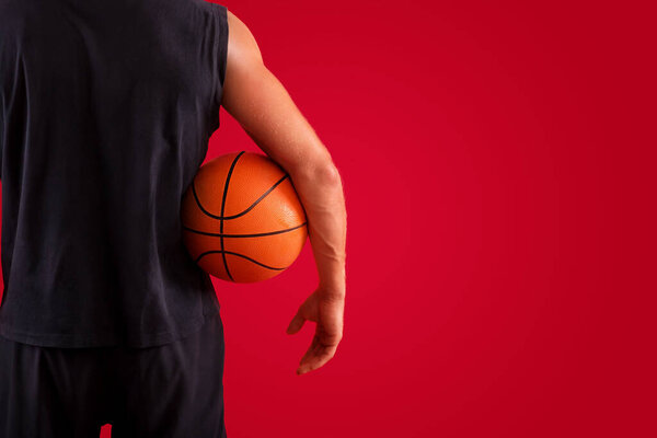 Closeup of millennial basketball player holding ball over red studio background, space for text