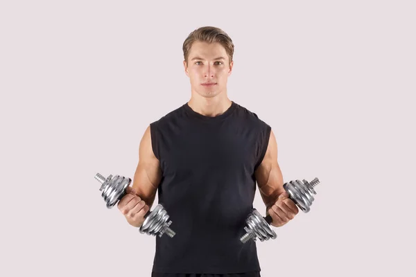 Portrait of motivated young weight lifter in sportswear working out with dumbbells on light studio background — Stock Photo, Image
