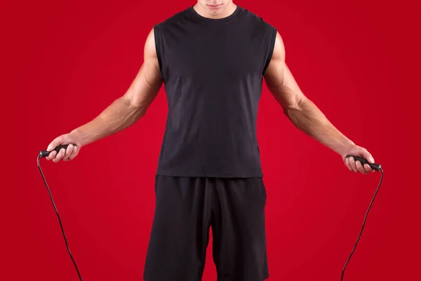 Cardio workout. Cropped view of millennial sportsman jumping on skipping rope on red studio background, closeup — Stock Photo, Image