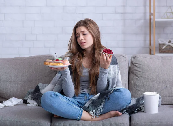 แนวคิดเรื่องการกินความผิดปกติ หญิงสาวที่เครียด กินของหวานบนโซฟาที่บ้าน รูปแบบเต็มความยาว — ภาพถ่ายสต็อก