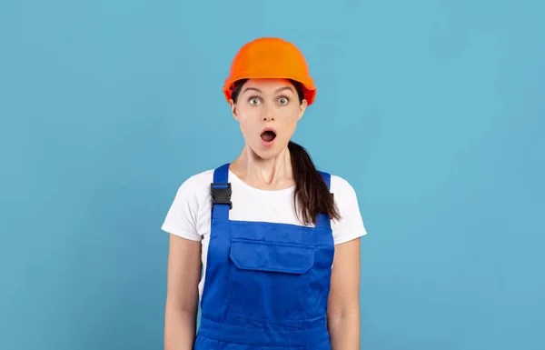 Πορτρέτο του Σοκαρίστηκε Handywoman σε Hardhat και Coveralls στέκεται πάνω από το μπλε φόντο — Φωτογραφία Αρχείου