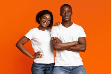 Gülümseyen siyah çift turuncu arka planda birlikte poz veriyor.