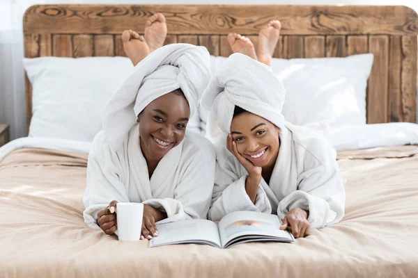 Sorrindo senhoras negras deitado na cama com caneca e revista — Fotografia de Stock