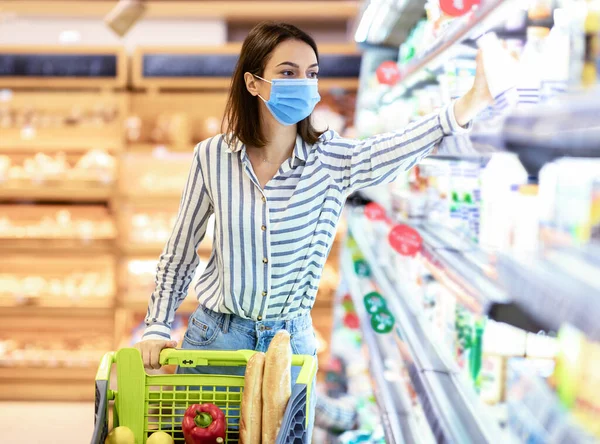 Woman in face mask shopping in supermarket with cart