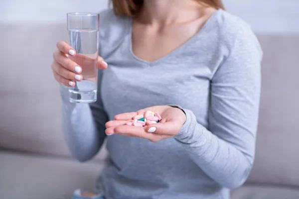 Mujer joven desesperada sosteniendo un puñado de pastillas y un vaso de agua, lista para suicidarse, primer plano — Foto de Stock