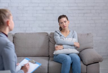 Sinir krizi geçiren umutsuz genç bir kadın psikolog ofisinde kanepede oturuyor ve yastığa sarılıyor.