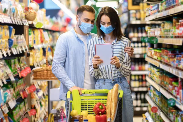 Ζευγάρι φορώντας μάσκες προσώπου σε Hypermarket, τον έλεγχο λίστα αγορών — Φωτογραφία Αρχείου