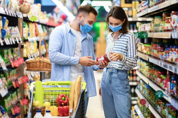 Young couple in protective masks shopping in supermarket — Stock Photo, Image