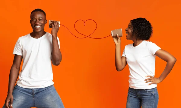 Jong zwart paar met kan telefoon op oranje achtergrond — Stockfoto
