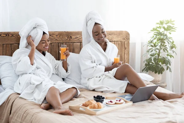 Mulheres negras alegres tomando café da manhã na cama, assistindo filme romântico — Fotografia de Stock