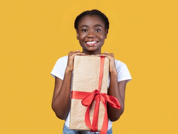 Vreugdevolle zwarte dame houden geschenken doos poseren over gele achtergrond — Stockfoto
