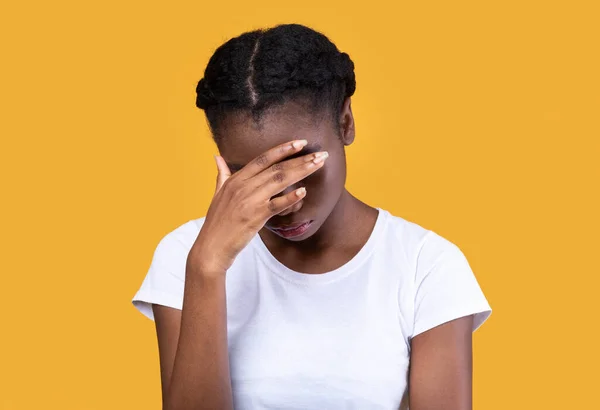 Deprimida mujer afroamericana cubriendo la cara sobre fondo de estudio amarillo —  Fotos de Stock