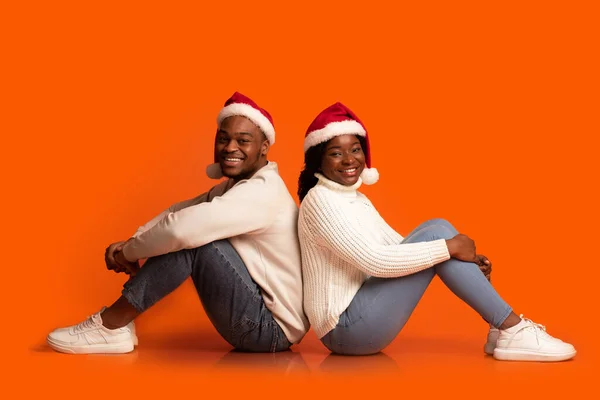 Retrato de alegre pareja negra en santa sombreros sentado espalda con espalda — Foto de Stock